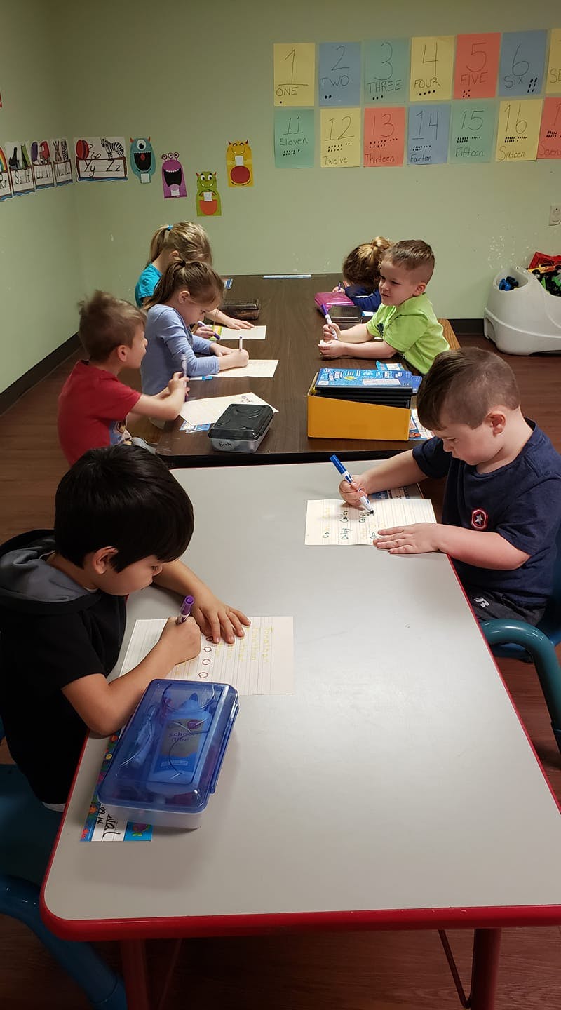 Children sitting at tables and writing in a classroom