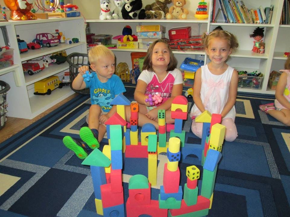 Three children sitting on a rug with colorful building blocks
