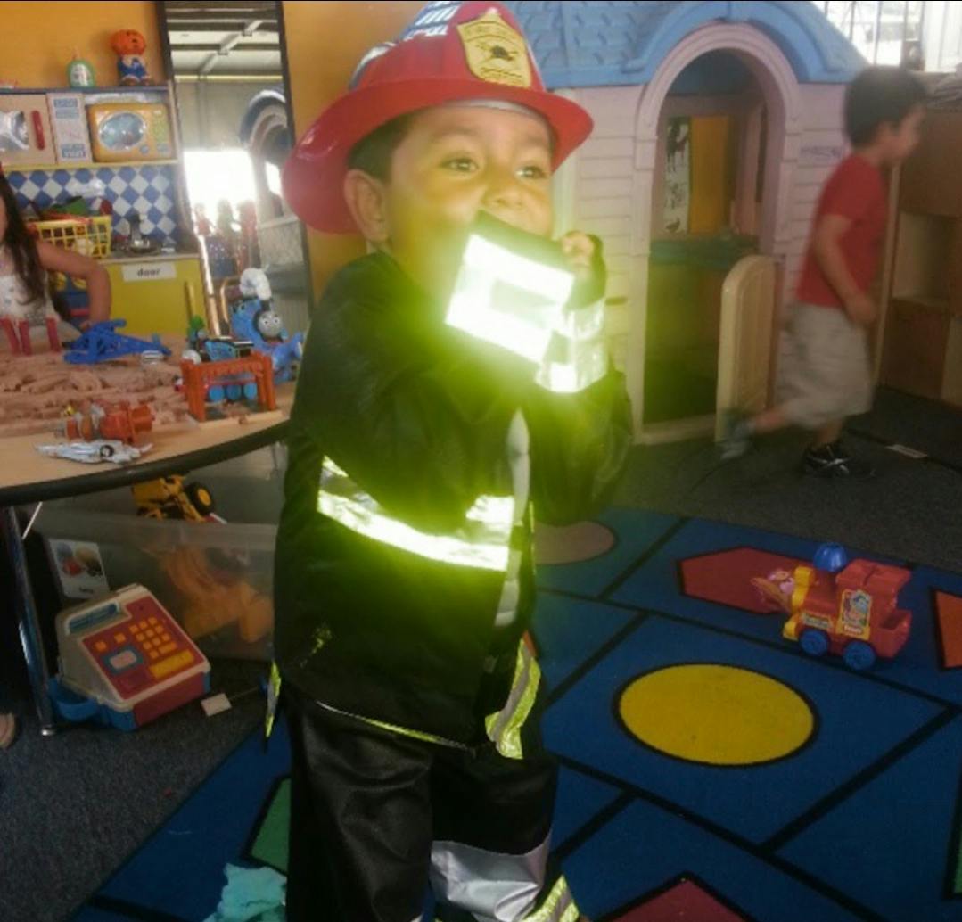 Child in firefighter costume holding a toy walkie-talkie