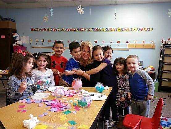 Adult and children gathered around a table with craft supplies in a classroom