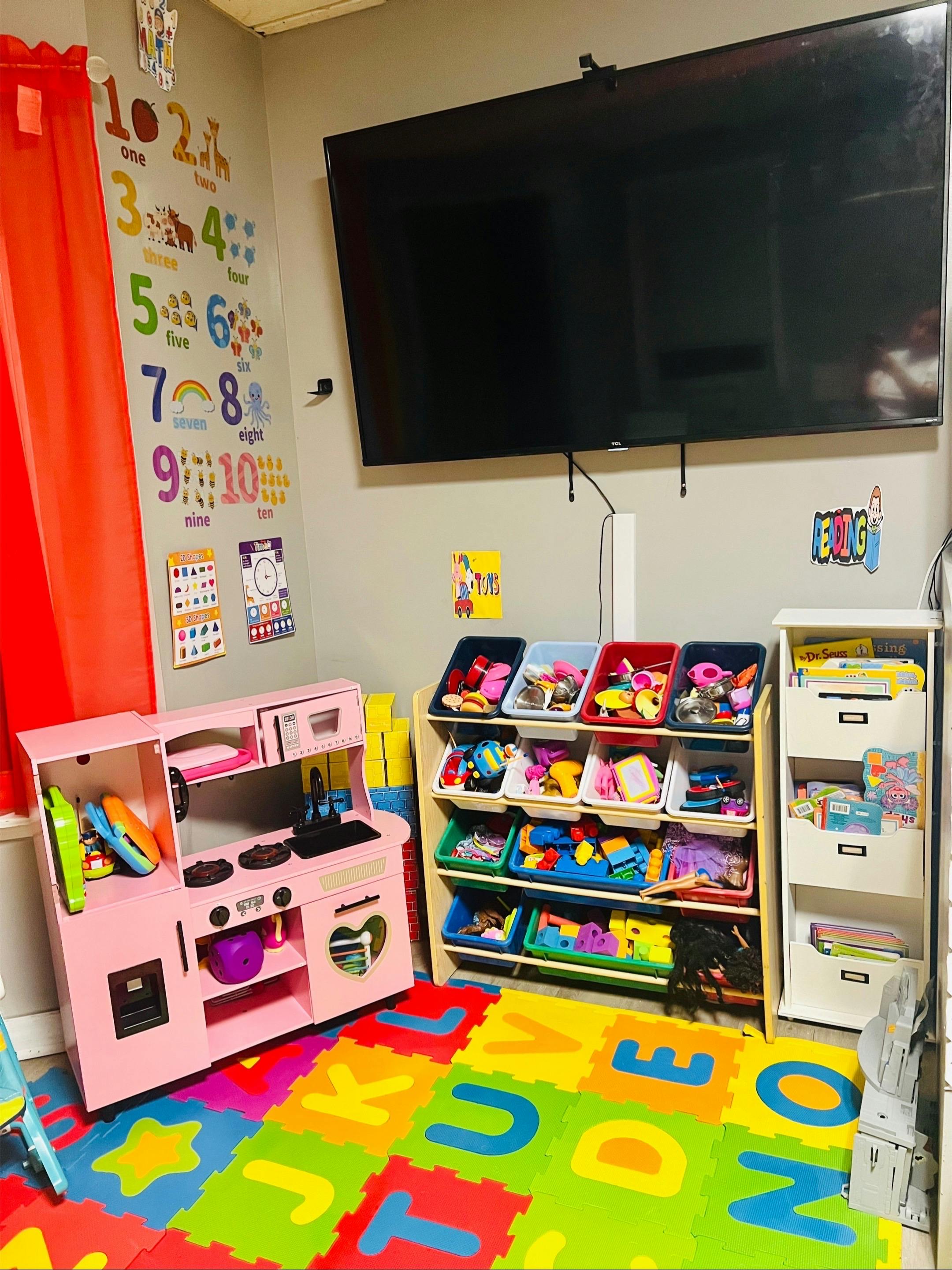 Playroom with a pink toy kitchen, toy storage, and alphabet floor mats