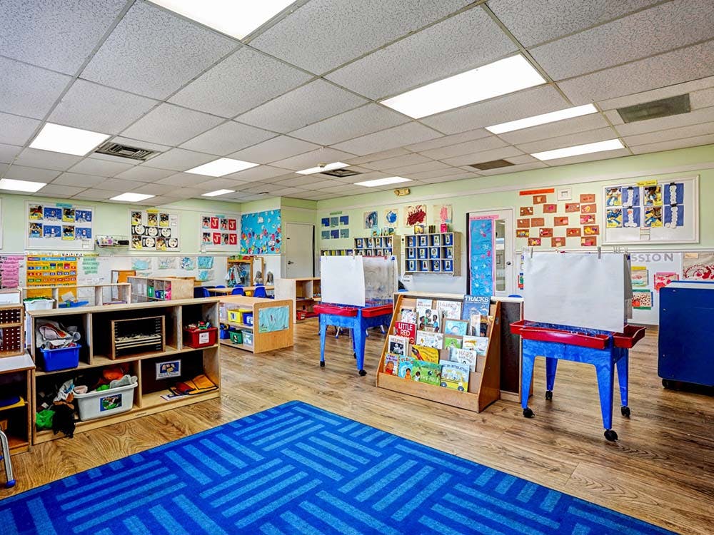 Empty classroom with a blue rug, wooden shelves, and children's artwork on the walls
