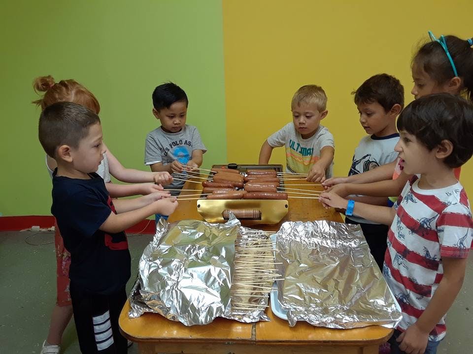 Children cooking hot dogs on a tabletop grill