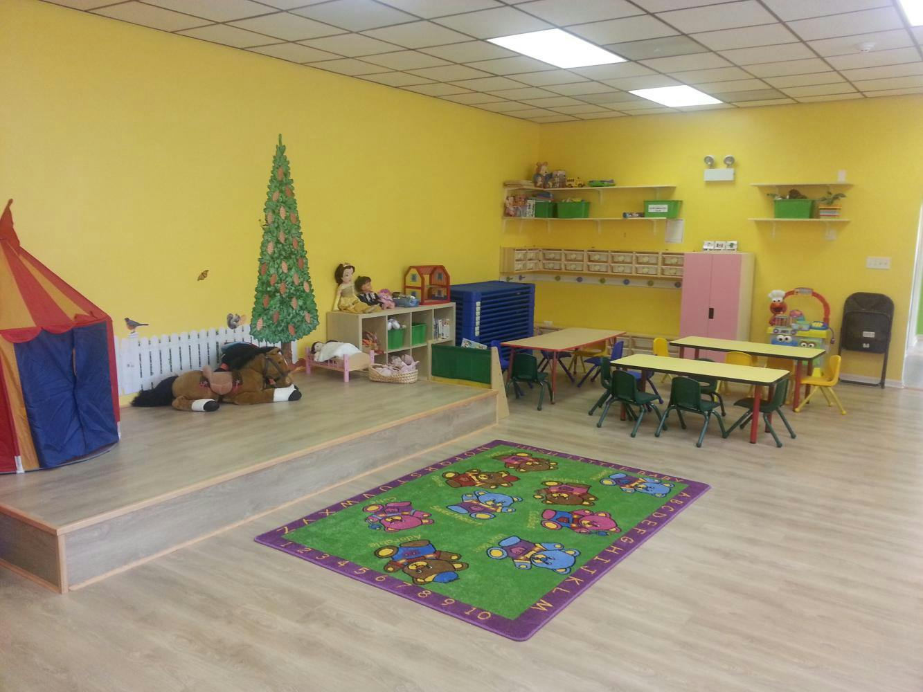 Playroom with small tables and chairs, a tent, and a green rug