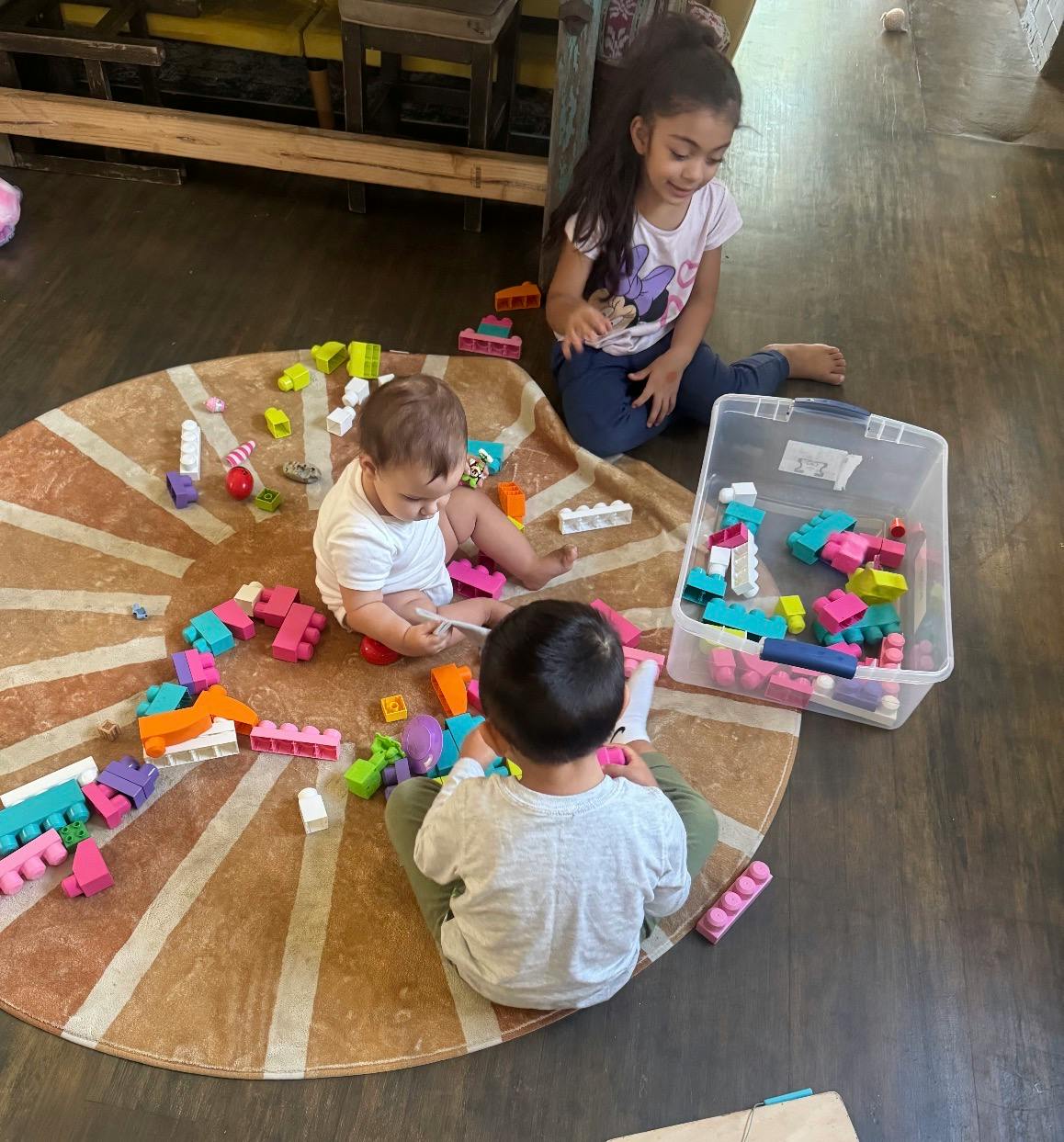 Three children playing with colorful building blocks on a round rug