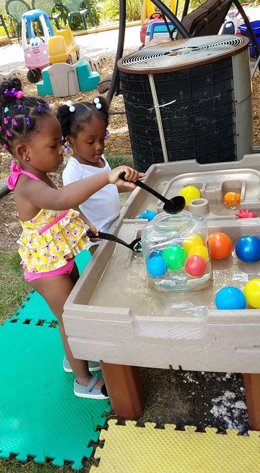 Two children playing with water and colorful balls in a water table