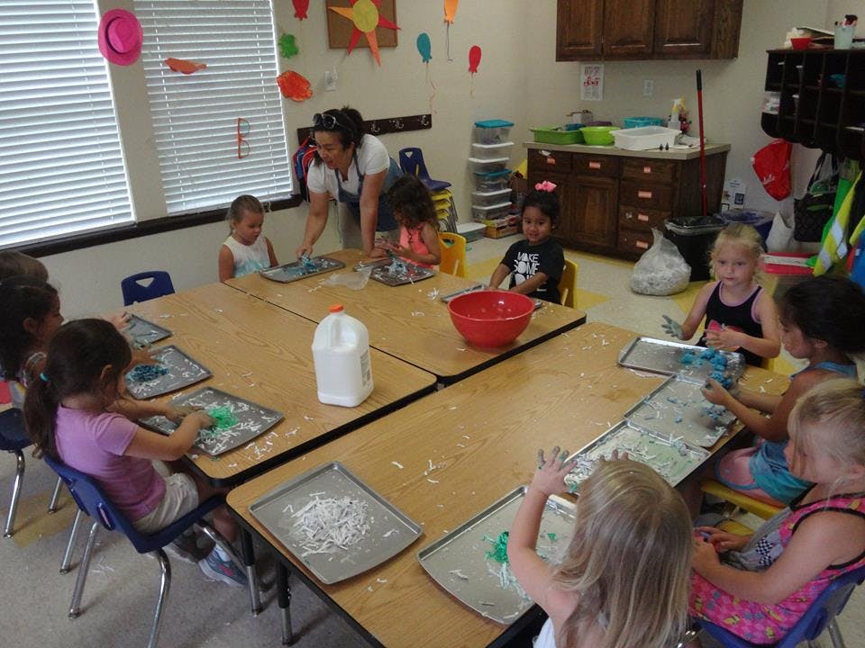 Adult and children doing an art activity at tables in a classroom