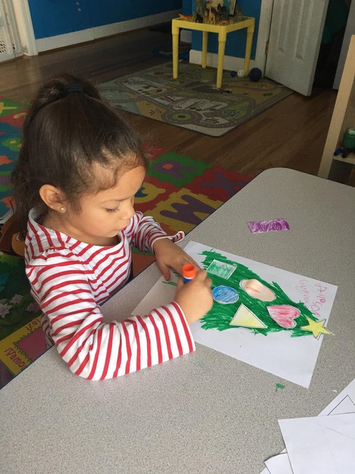 Child gluing shapes onto a drawing of a Christmas tree