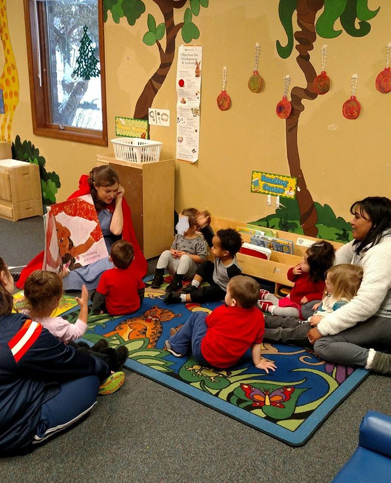 Adult reading a book to a group of children in a classroom