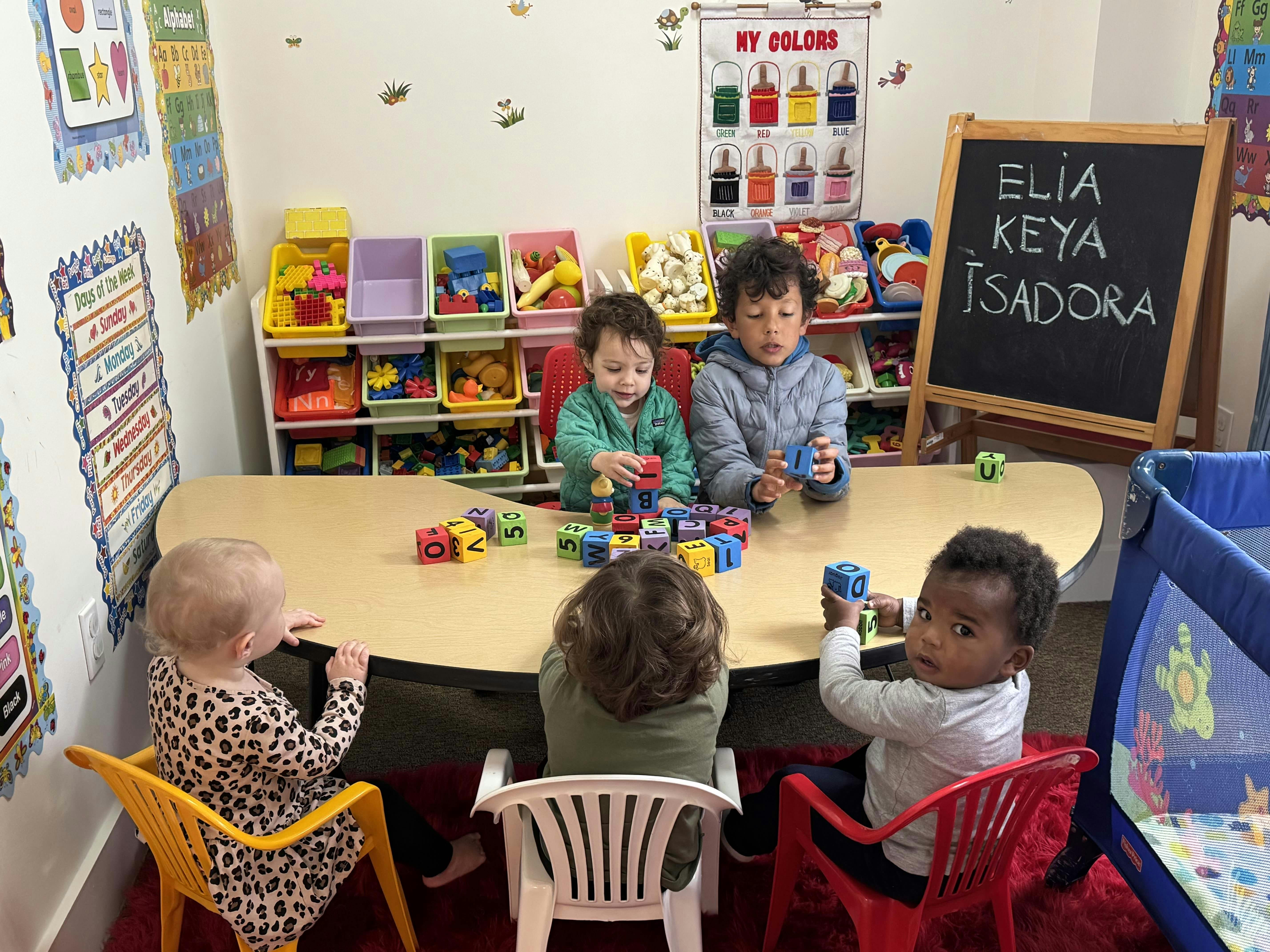 Five children playing with alphabet blocks at a table in a classroom