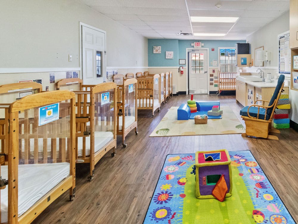 A room with multiple cribs, play mats, and a changing station