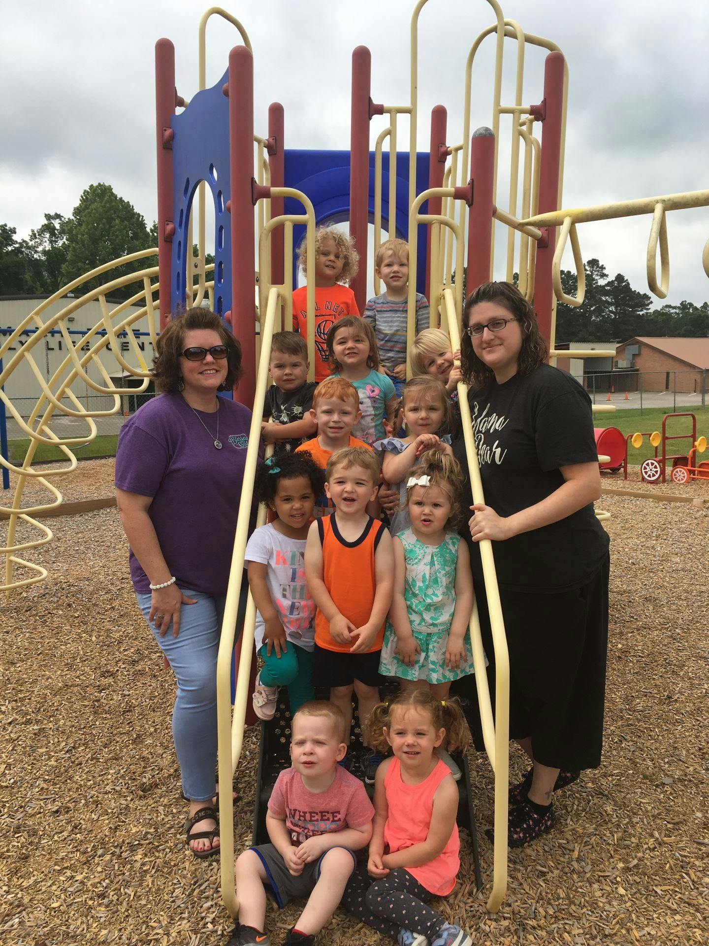 Two people with a group of children on playground equipment