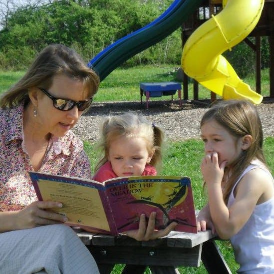 Person reading a book to two children outdoors