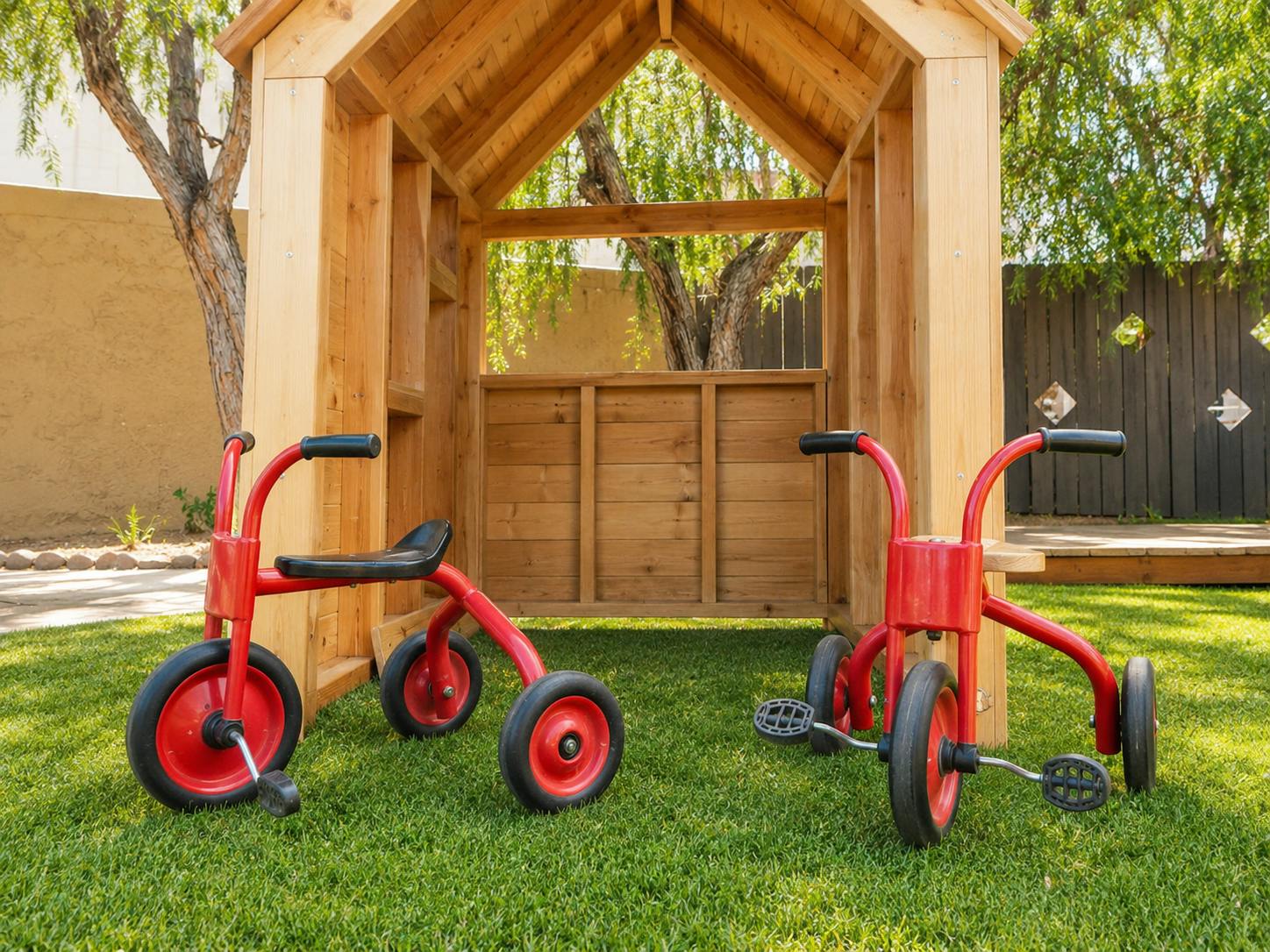 Two red tricycles parked in front of a wooden playhouse on a lawn