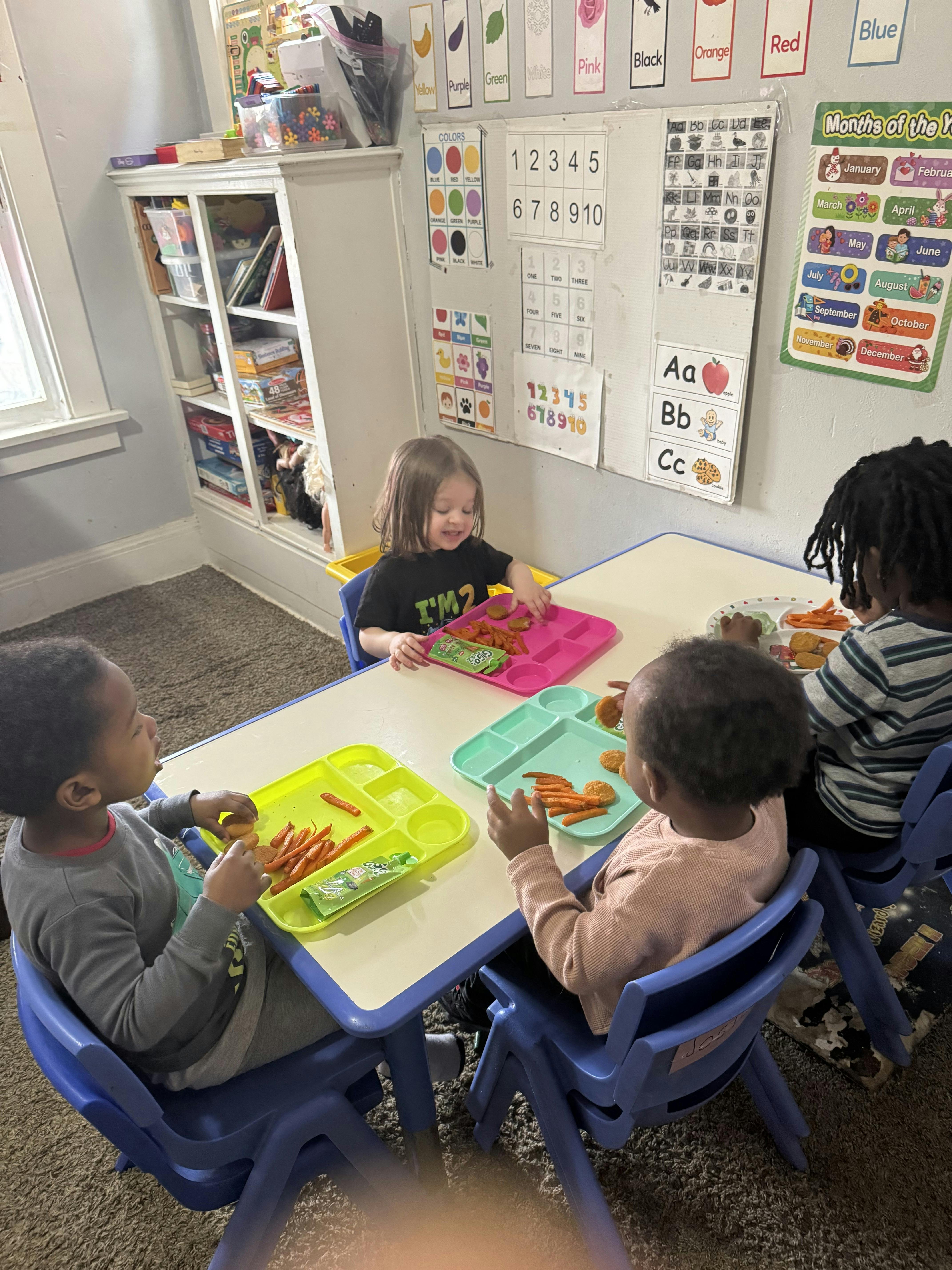 Four children eating snacks at a small table in a classroom