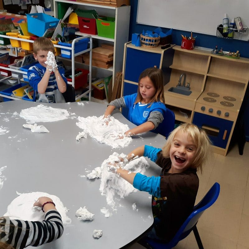 Children playing with white dough on a table in a classroom