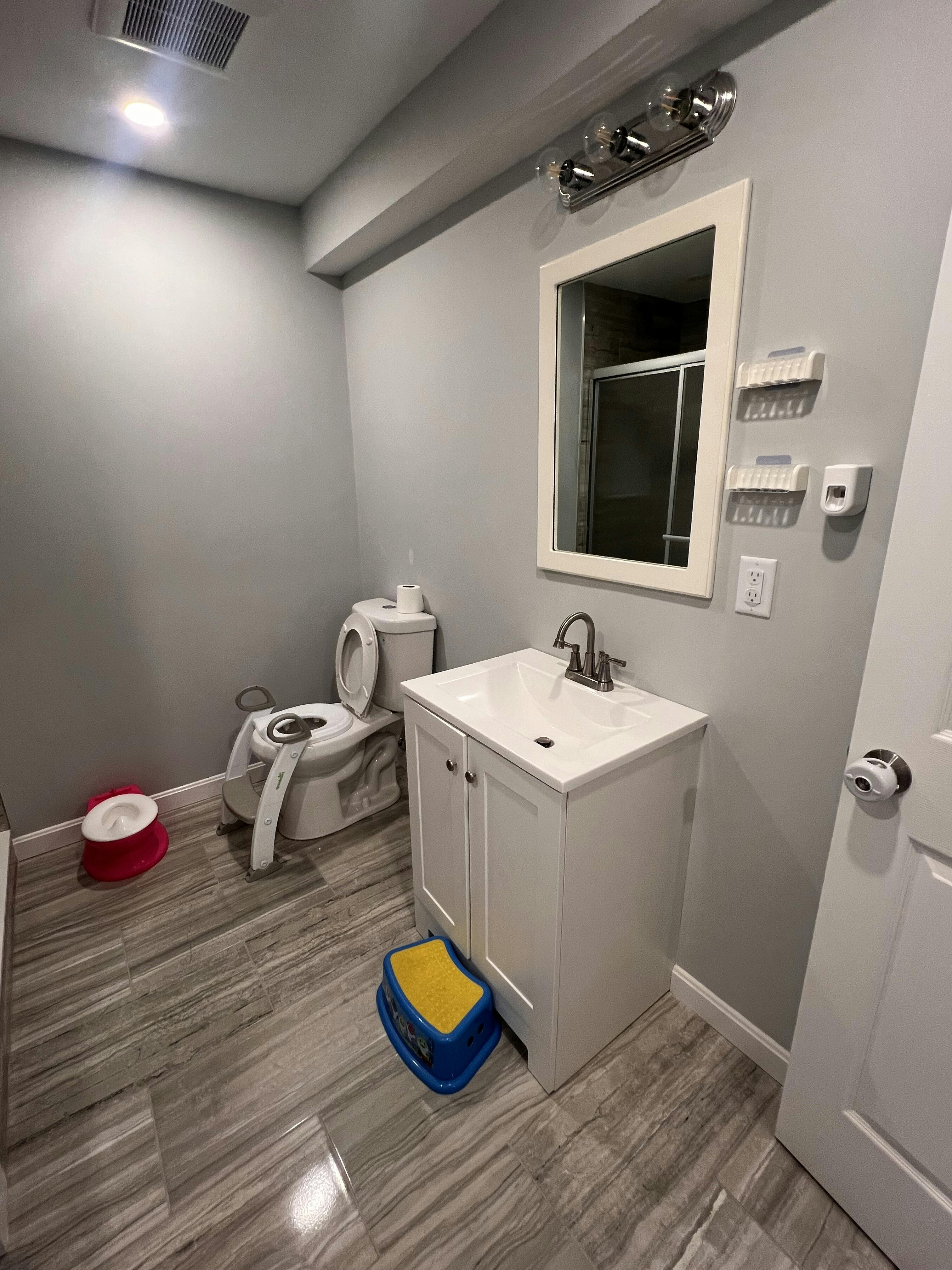 Bathroom with toilet, sink, mirror, and child's potty training accessories