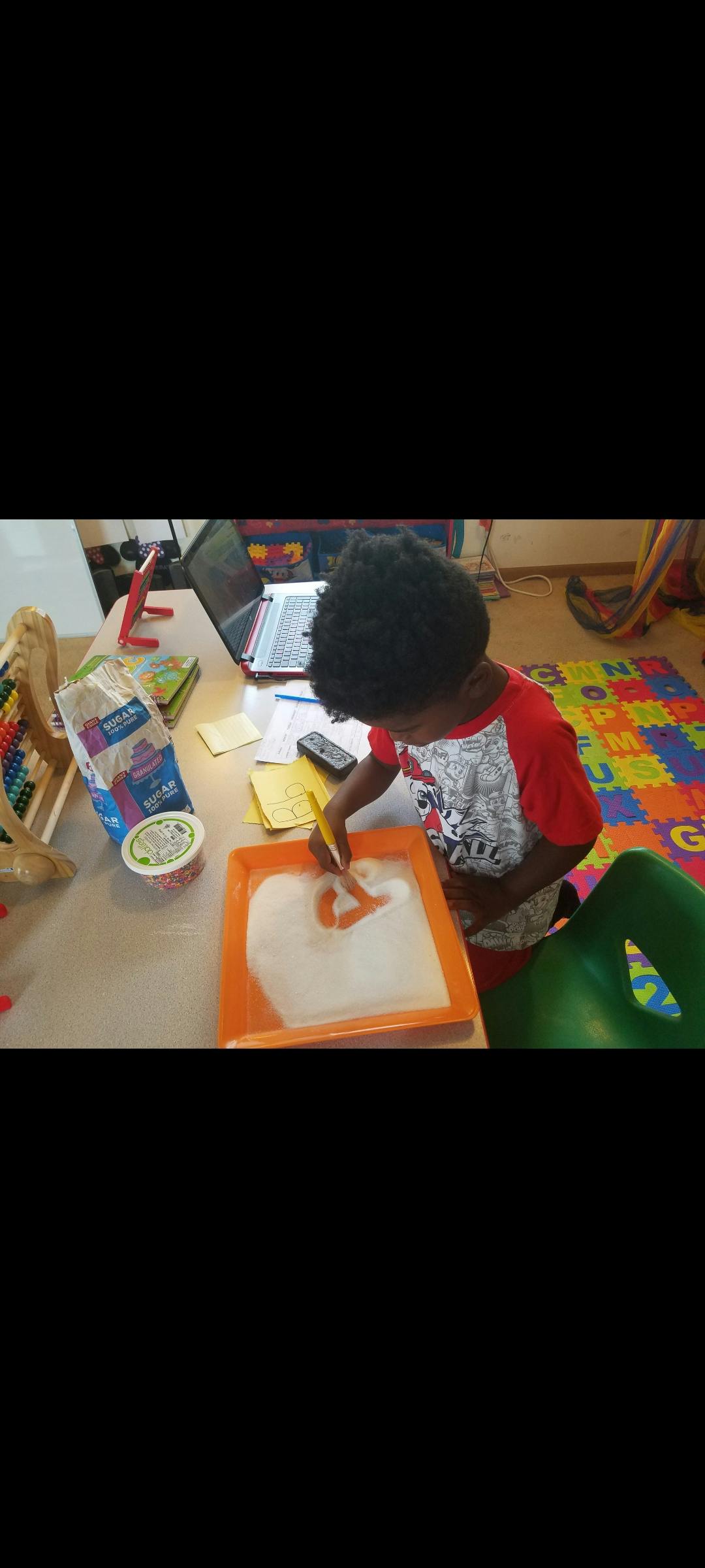 Child drawing in a sand tray with a yellow tool