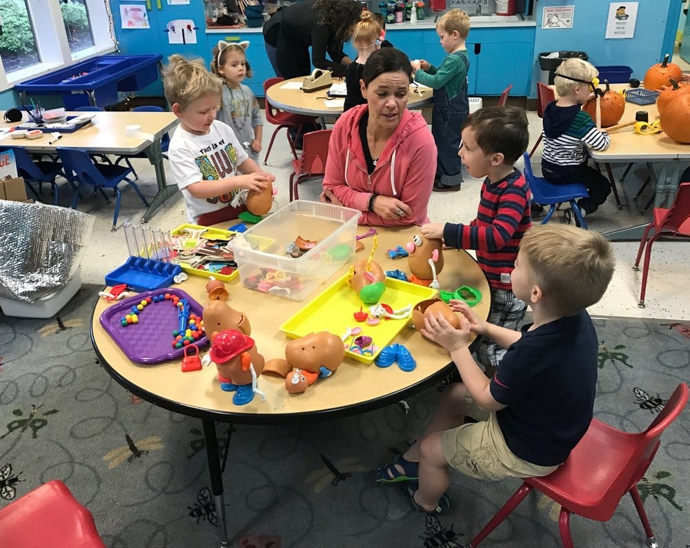 Adult and children playing with toys at a table in a classroom