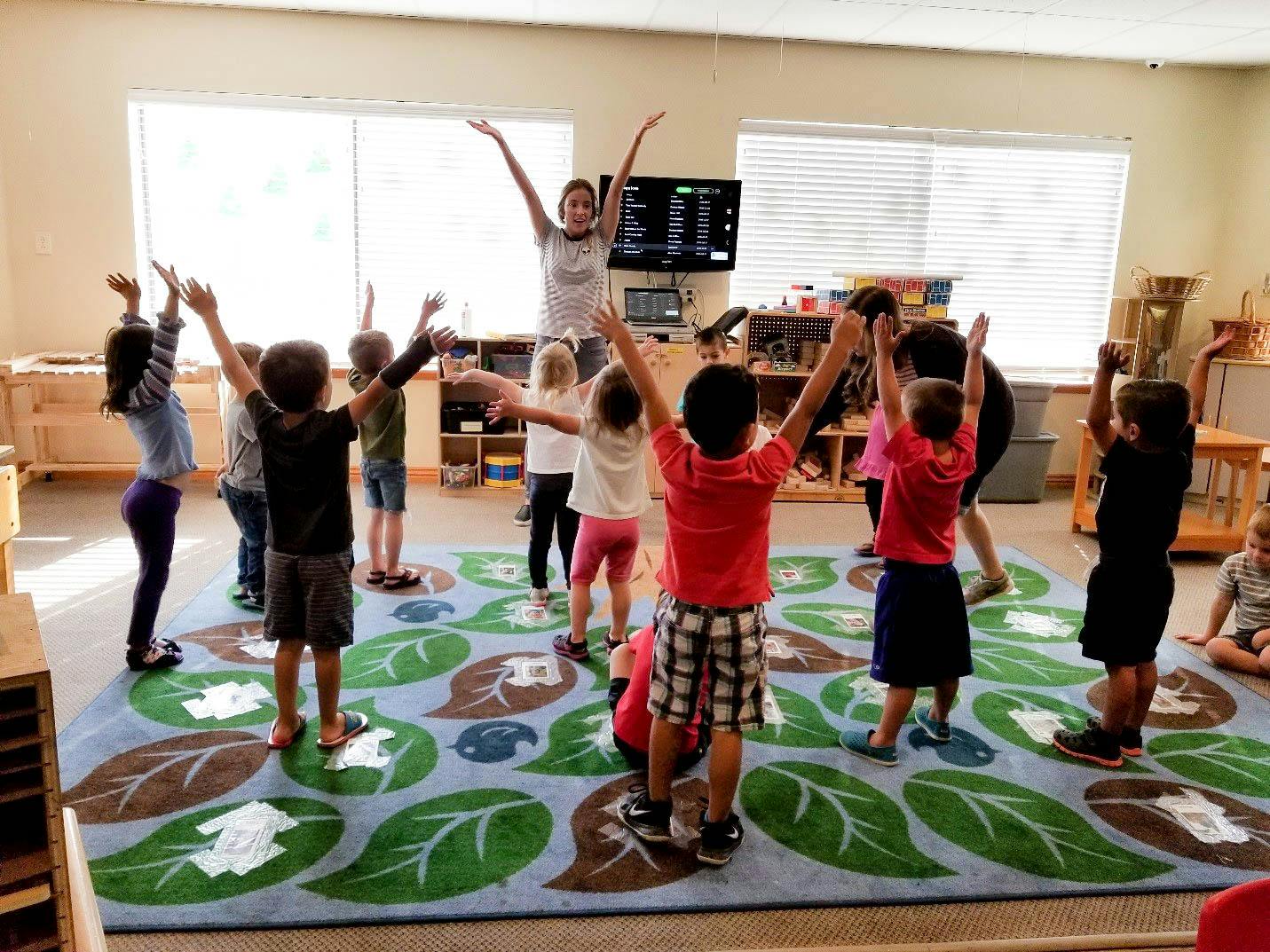 Adult and children with arms raised in a classroom