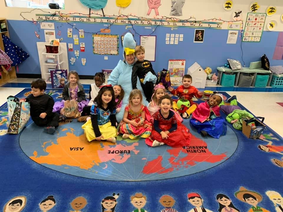Person in costume with children in costumes sitting on a world map rug in a classroom
