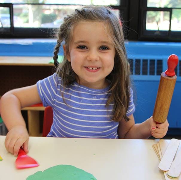 Child holding a rolling pin and a scraper at a table