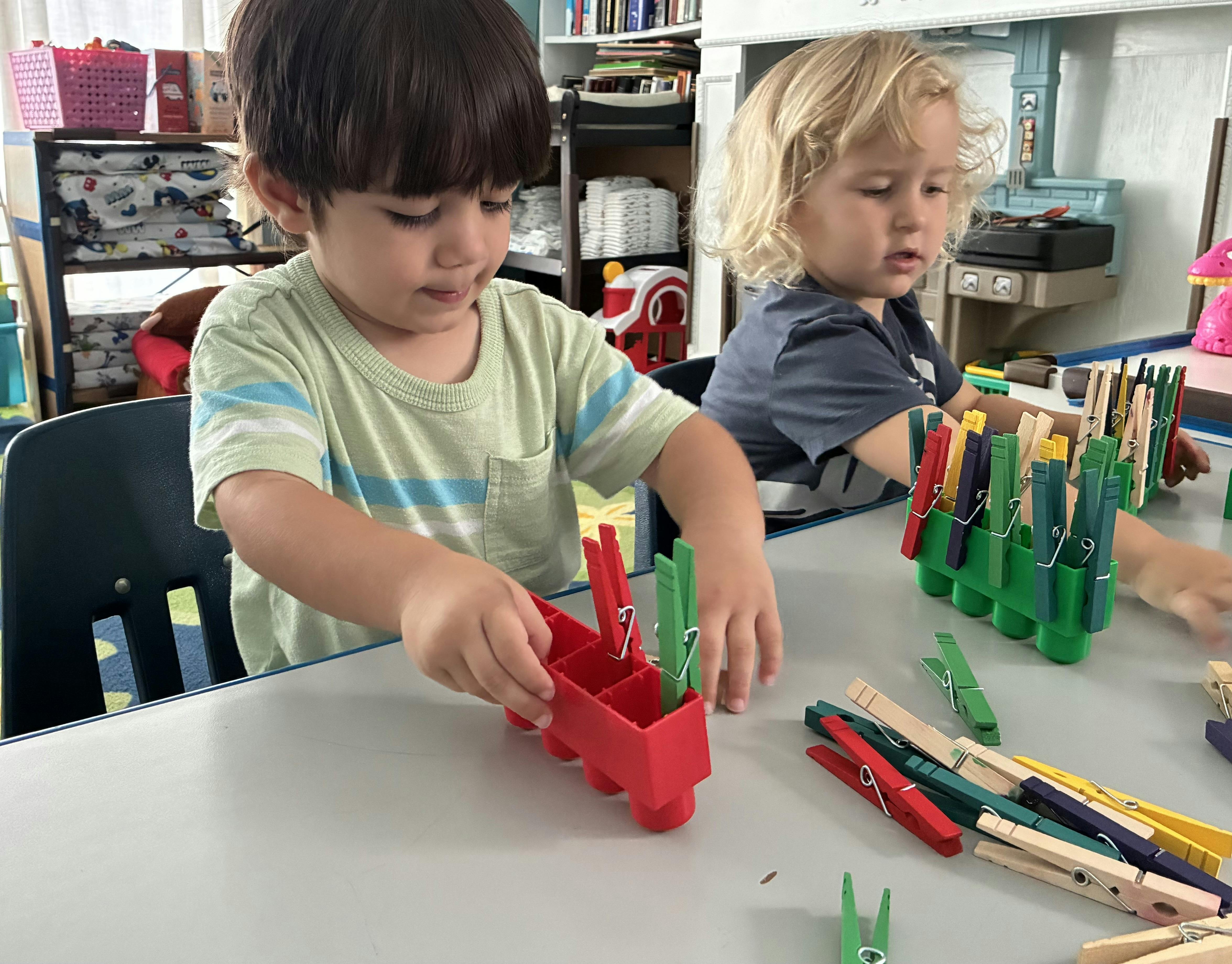Two children playing with colorful clothespins at a table