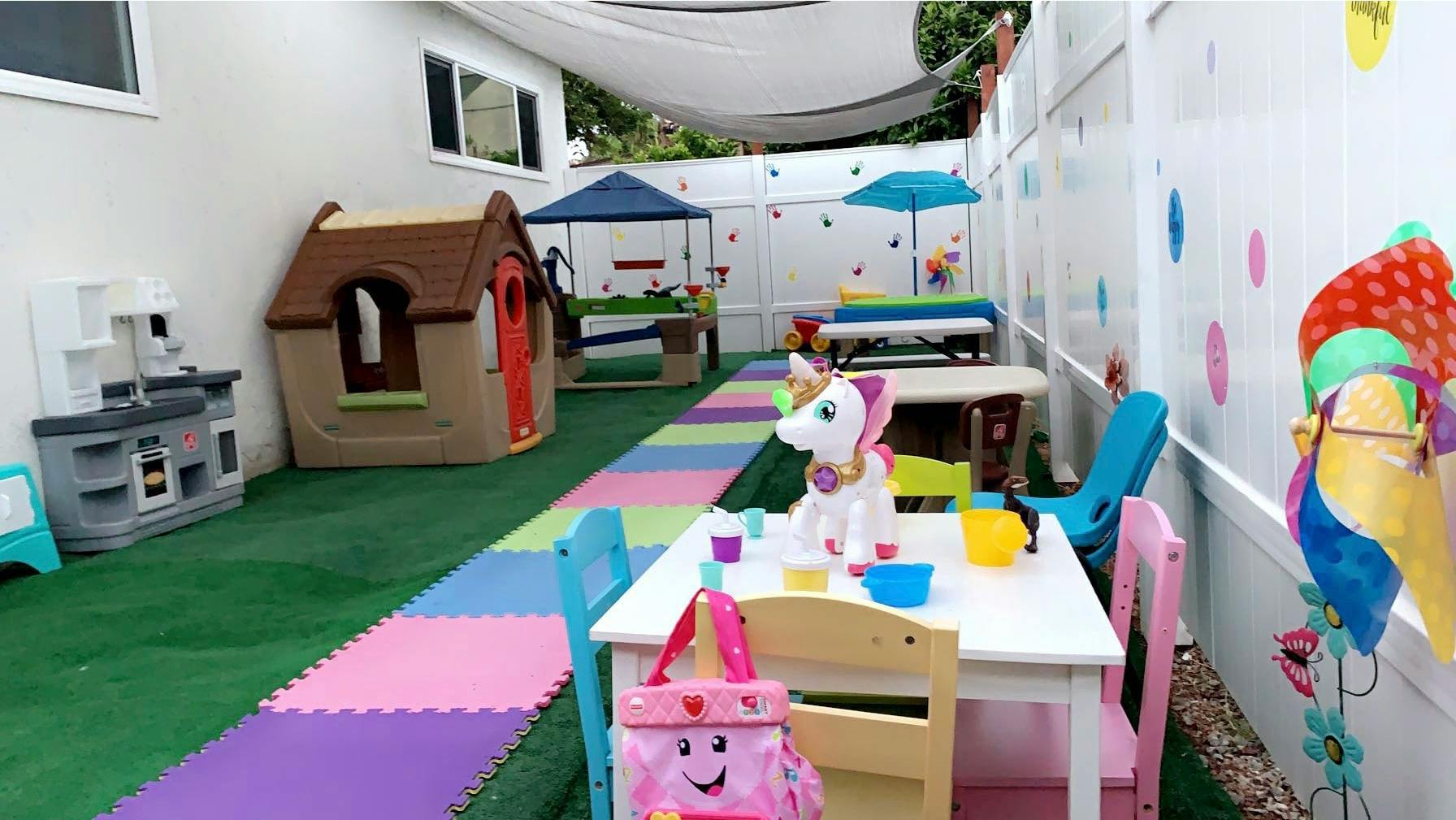 Outdoor play area with playhouses, tables, and colorful floor mats