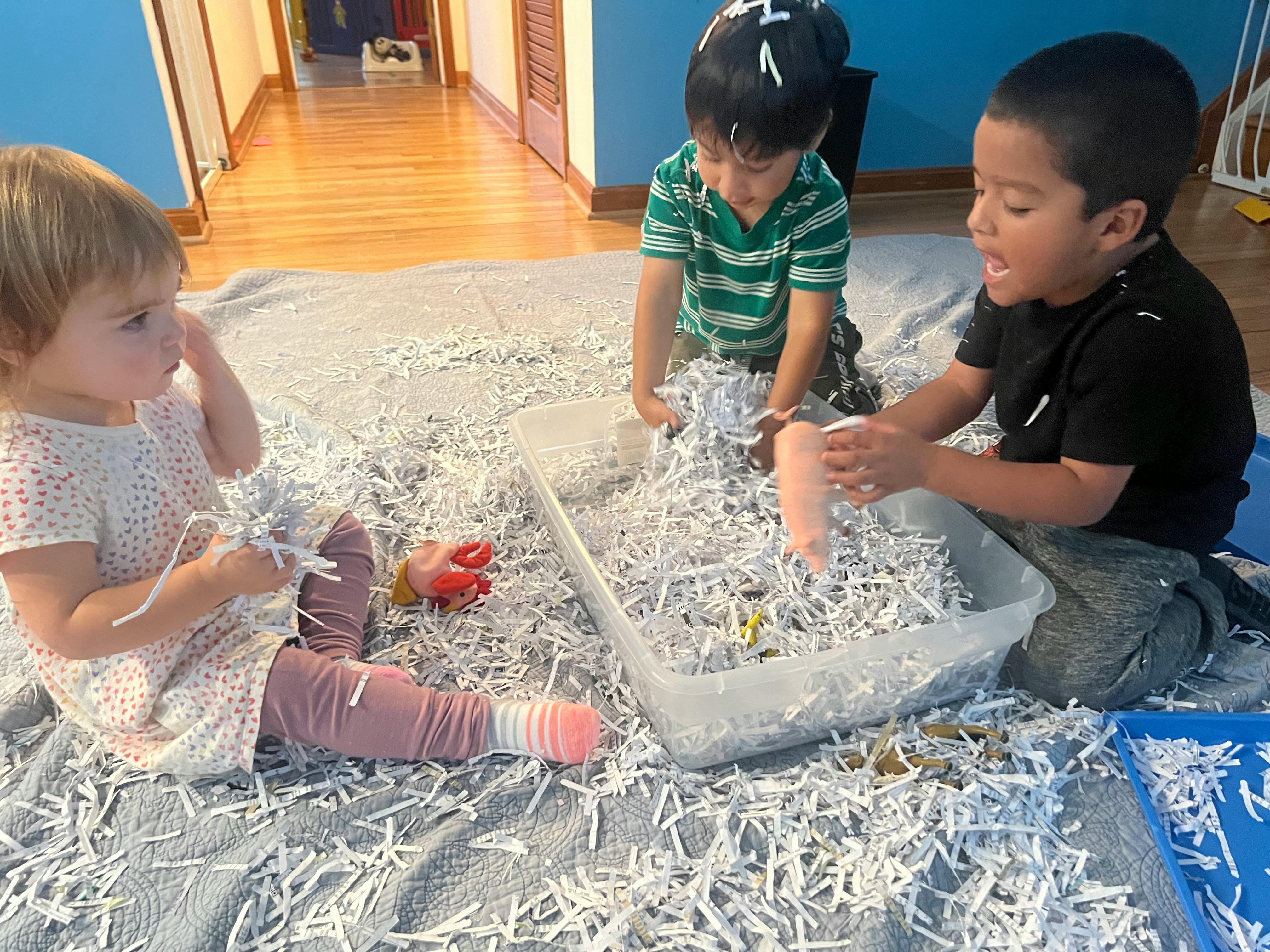 Three children playing with shredded paper on the floor