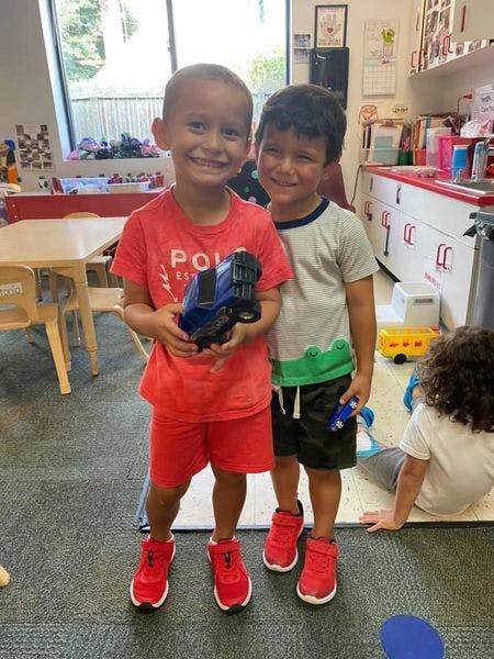 Two children standing and smiling, one holding a toy truck