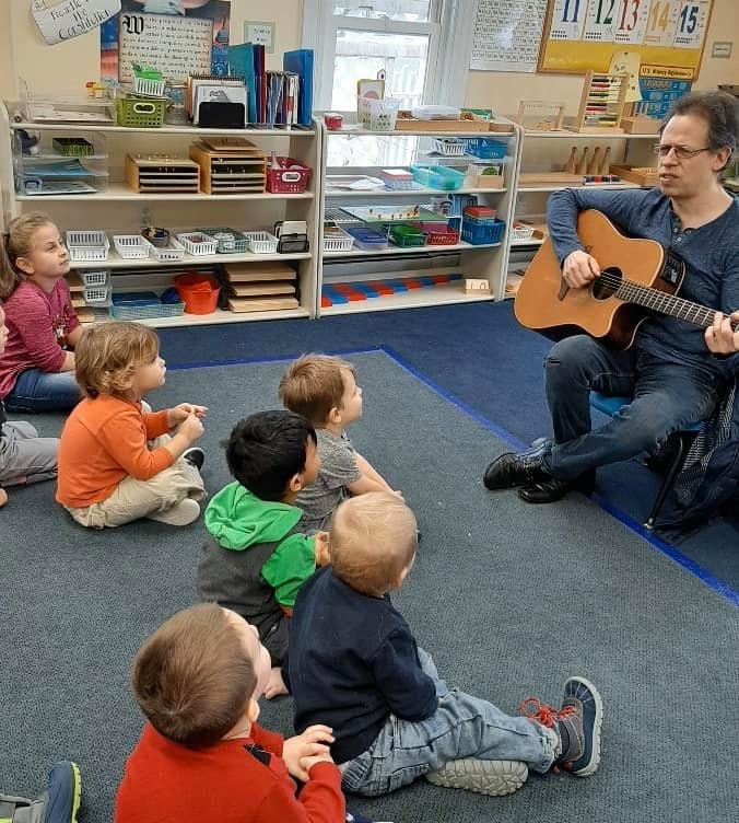 Person playing guitar for a group of children in a classroom