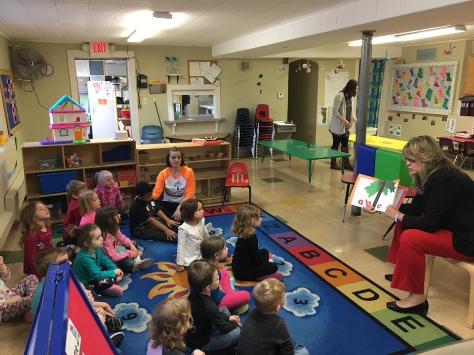 Adult reading a book to a group of children in a classroom