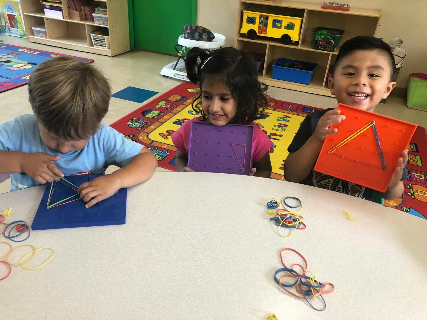 Three children playing with rubber bands and geo boards at a table