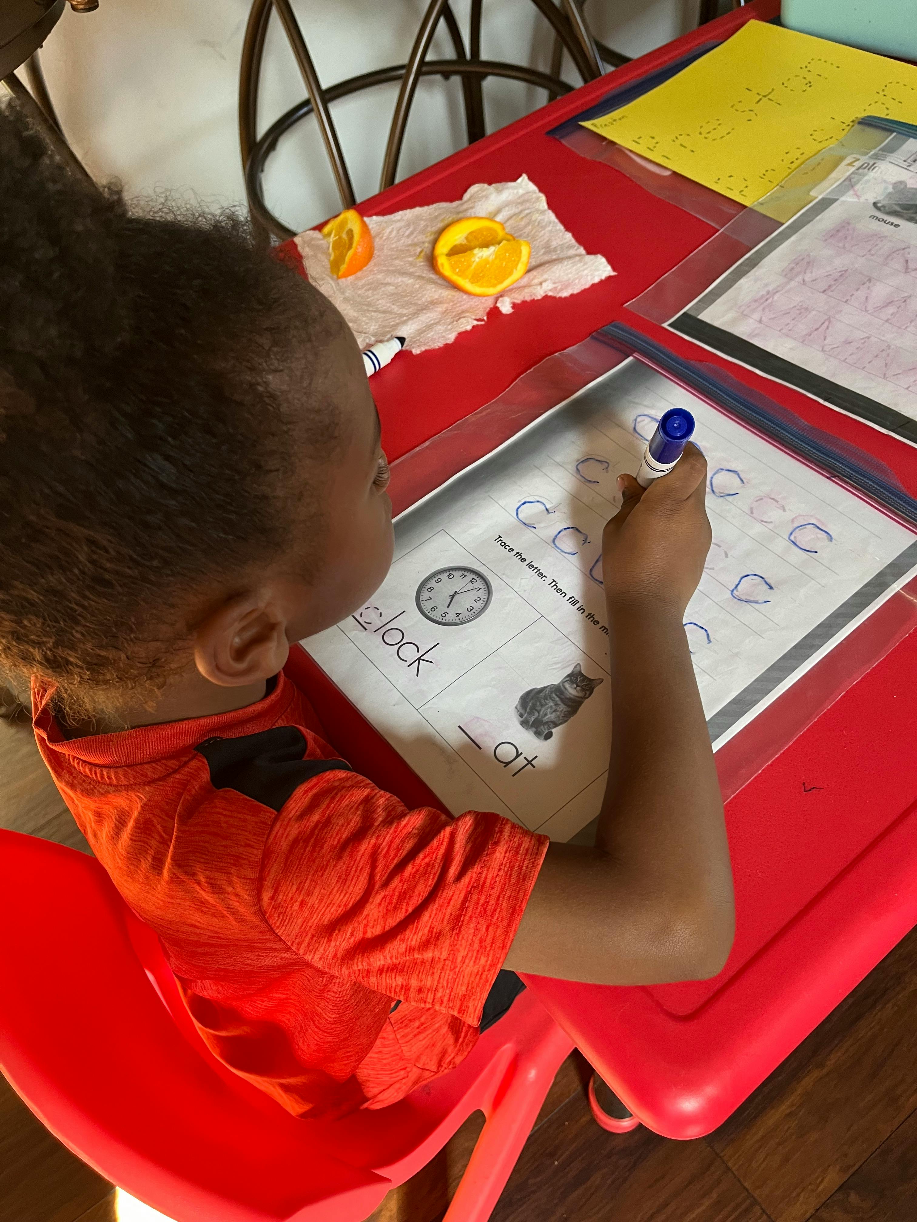 Child writing on a worksheet at a red table