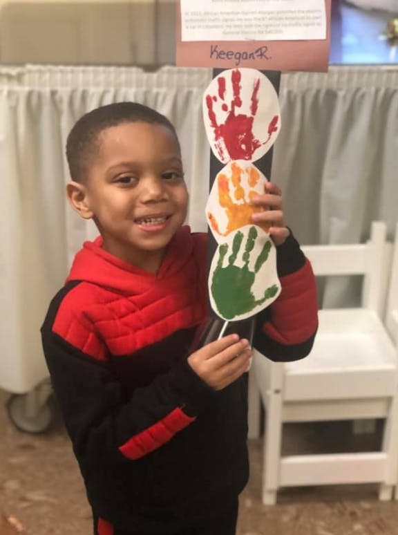 Child holding a craft stick with three handprints in print cutouts