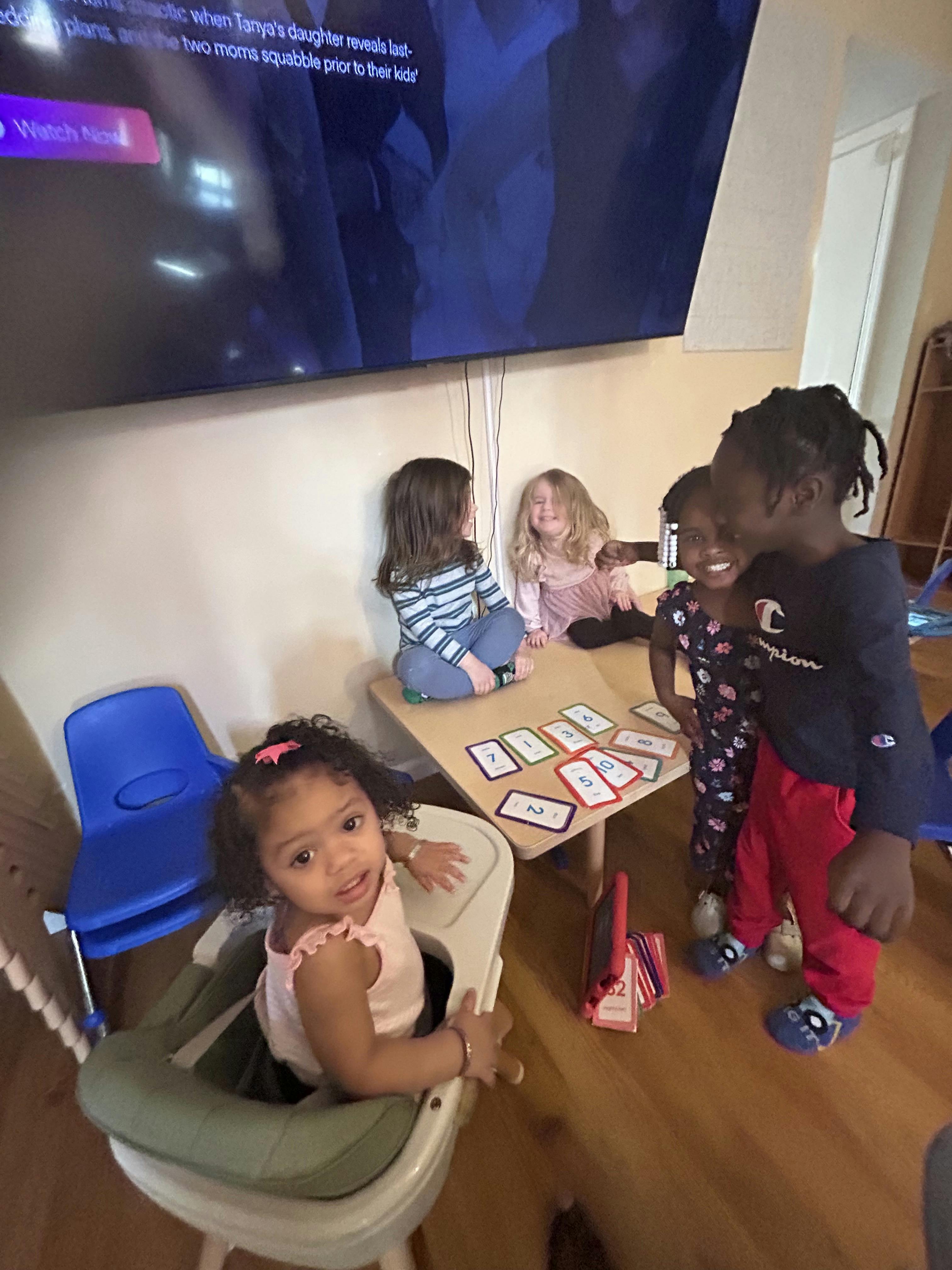 Children playing with cards at a small table, one child in a high chair