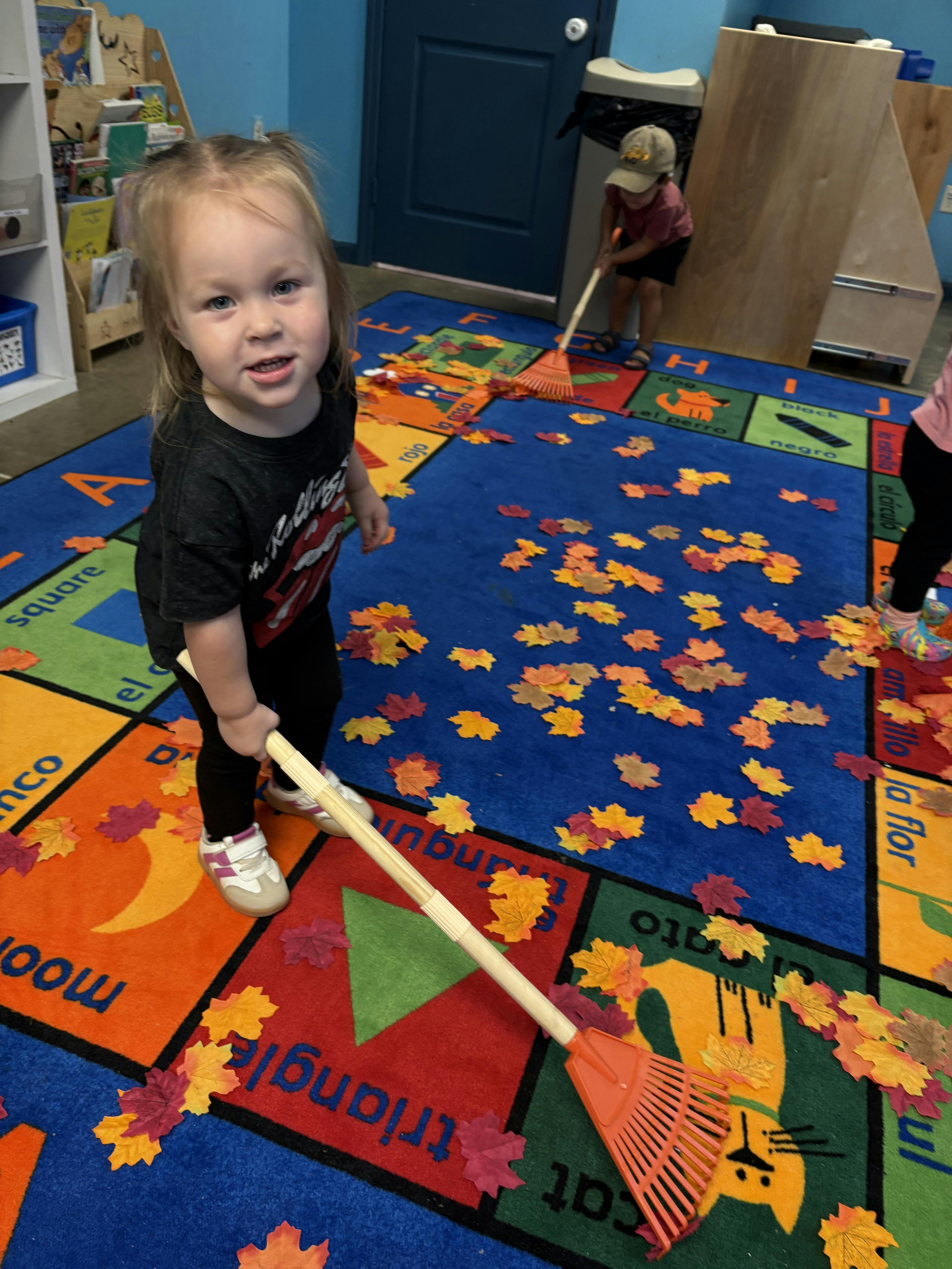 Child holding a toy rake on a colorful rug with artificial leaves