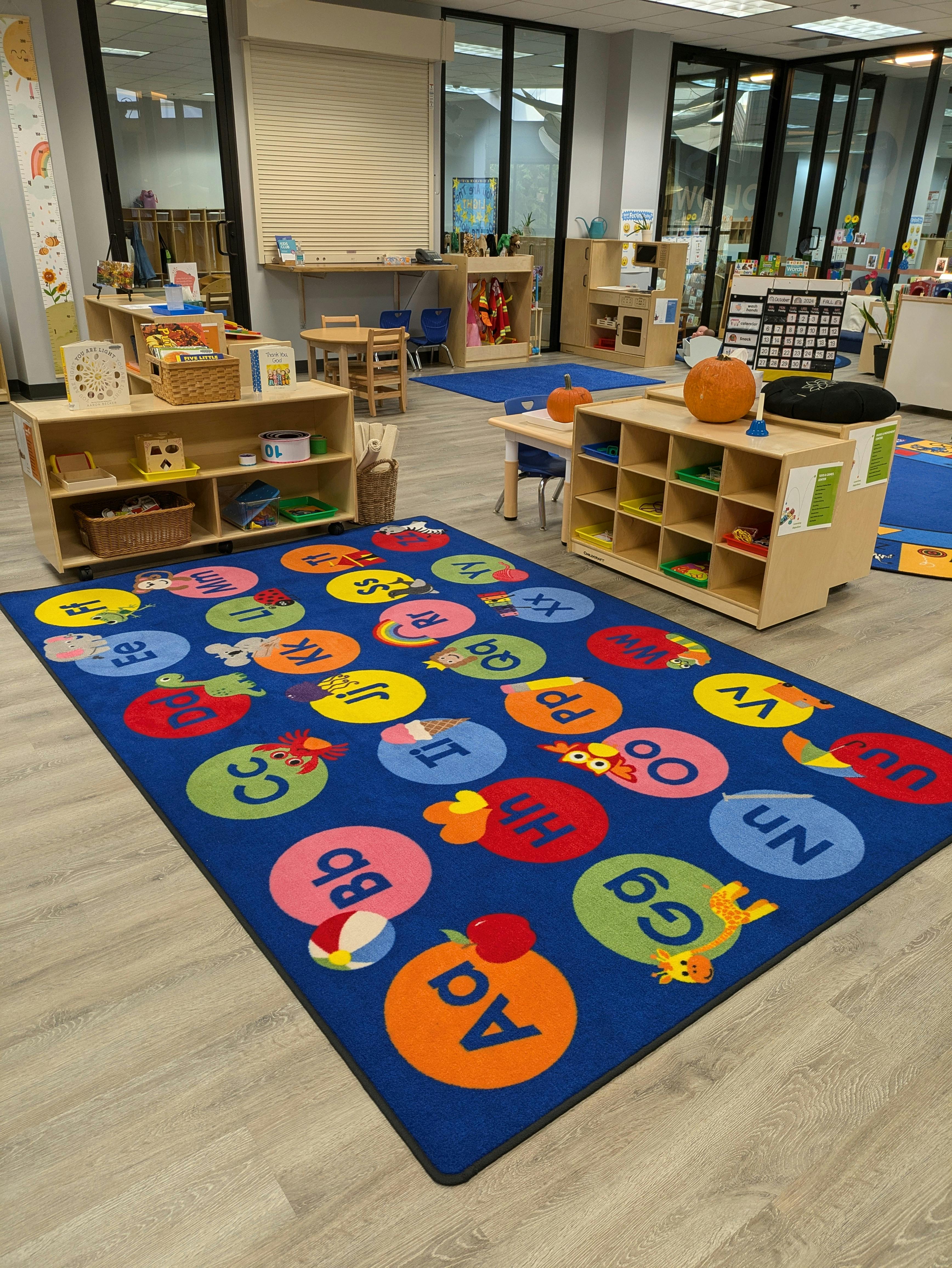 Classroom with a blue alphabet rug and wooden shelves