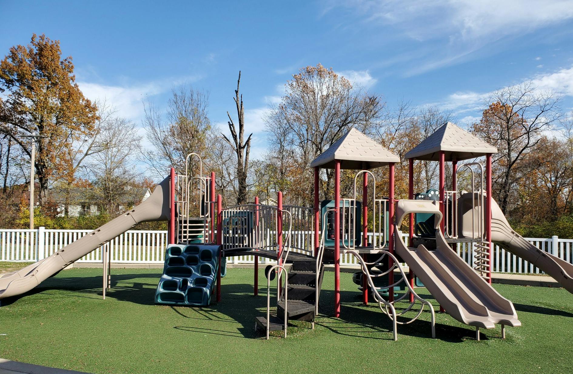 Playground with slides, climbing structures, and a white fence