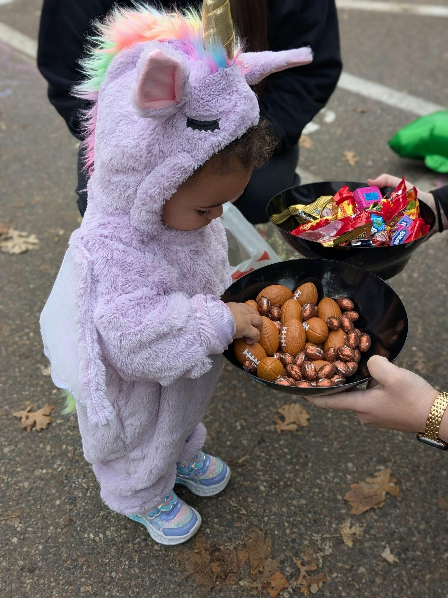 Child in a unicorn costume picking small football toys from a bowl