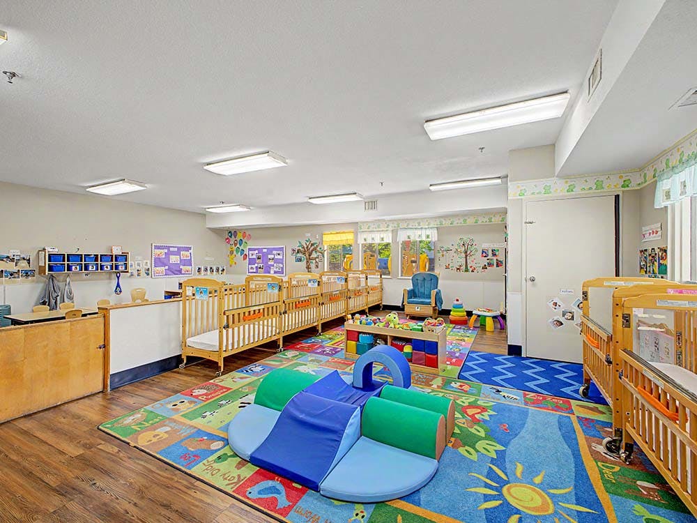 A colorful daycare room with several cribs, playmats, and children's furniture