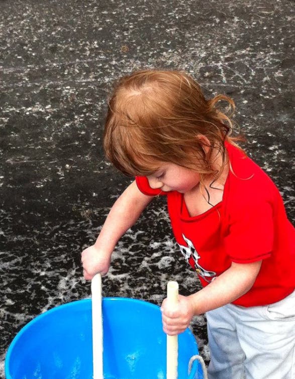 Child stirring a blue bucket with two sticks
