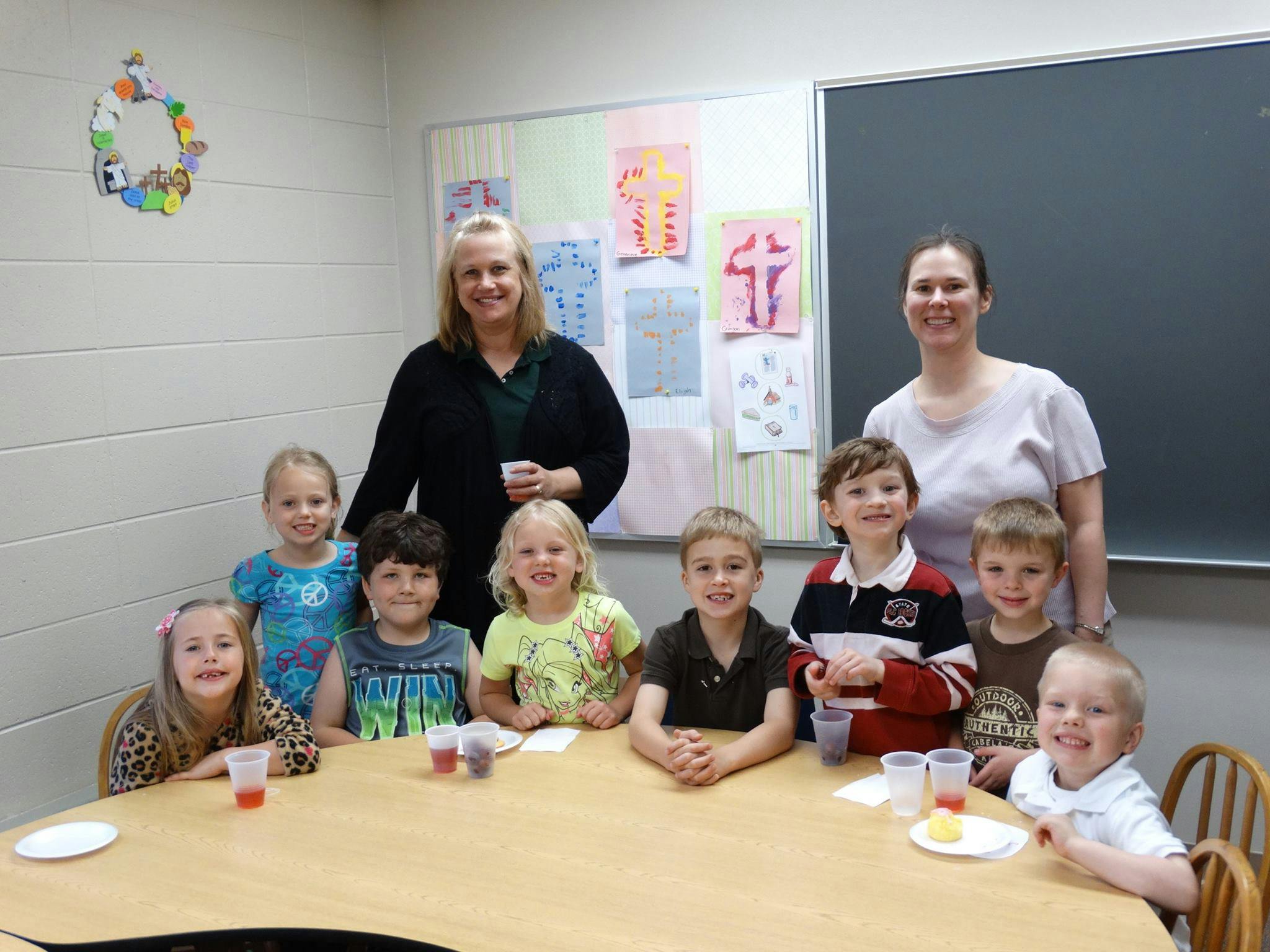 Two adults and multiple children gathered around a table in a classroom