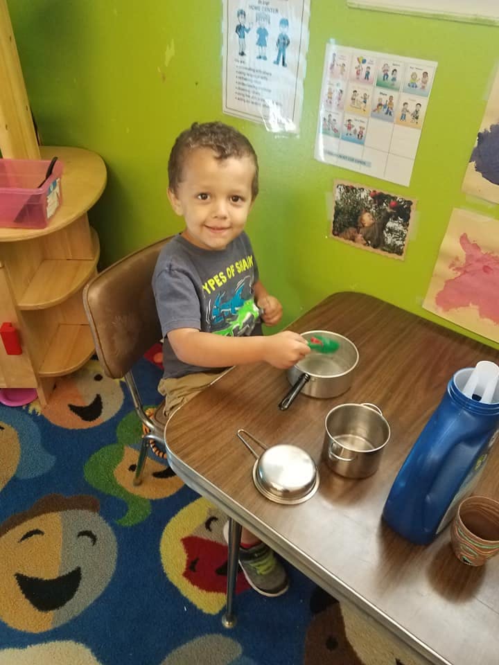 Child sitting at a table with toy pots and pans