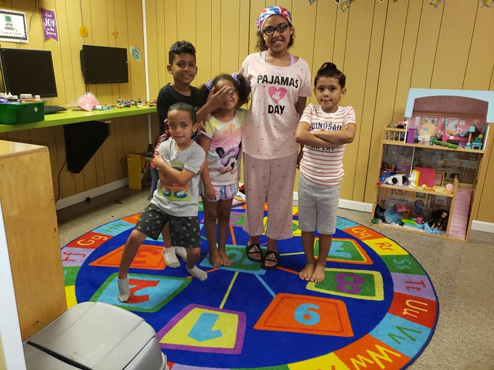 Group of children and one adult standing on a colorful rug