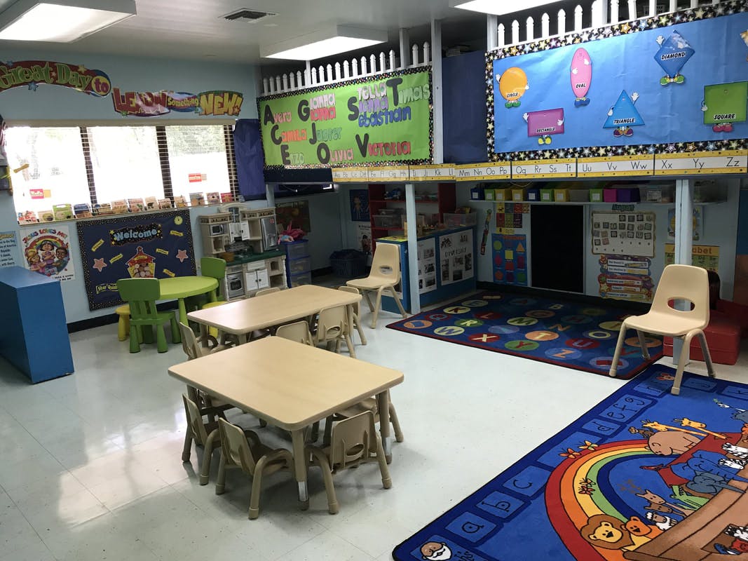Classroom with small tables and chairs, colorful rugs, and educational posters