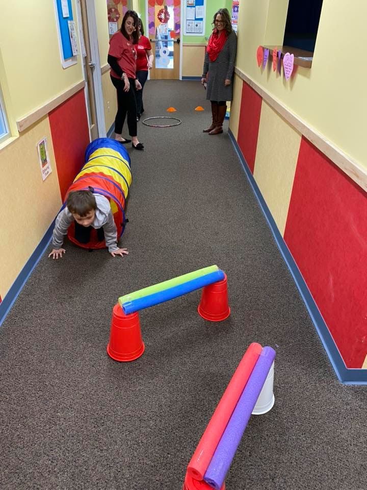 Child crawling through a colorful tunnel in a hallway with adults watching