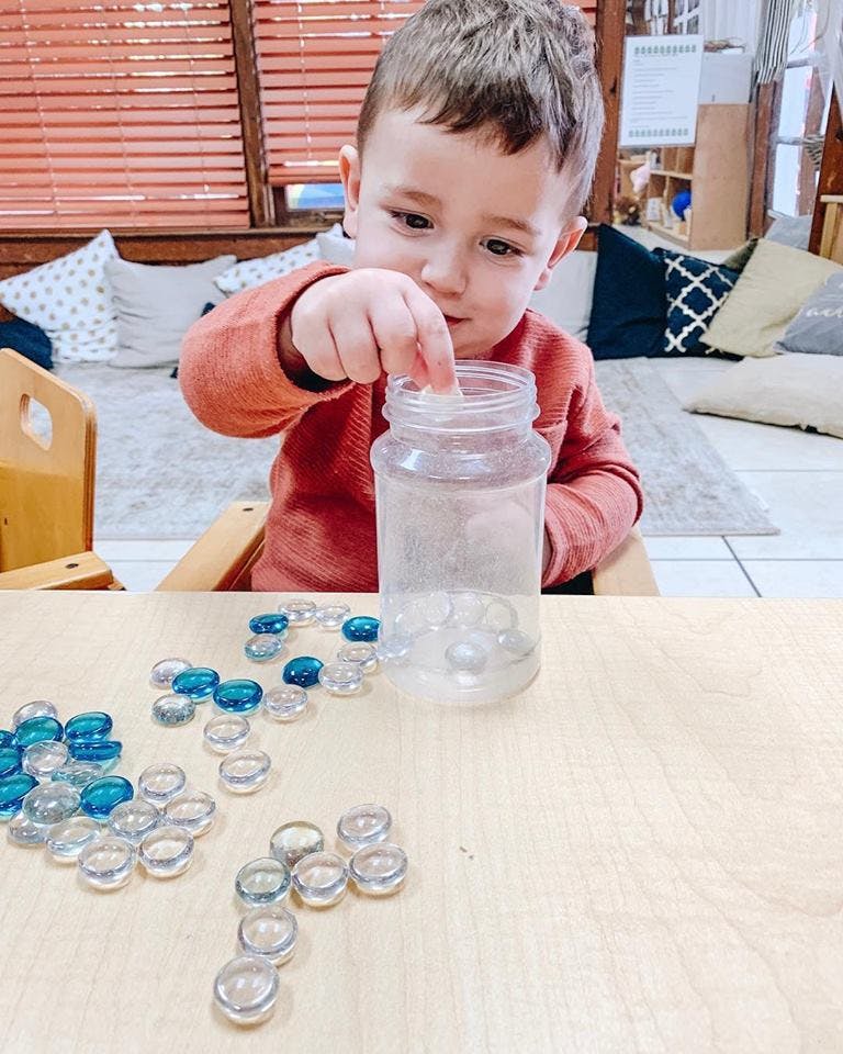 Child putting clear and blue glass pebbles into a jar