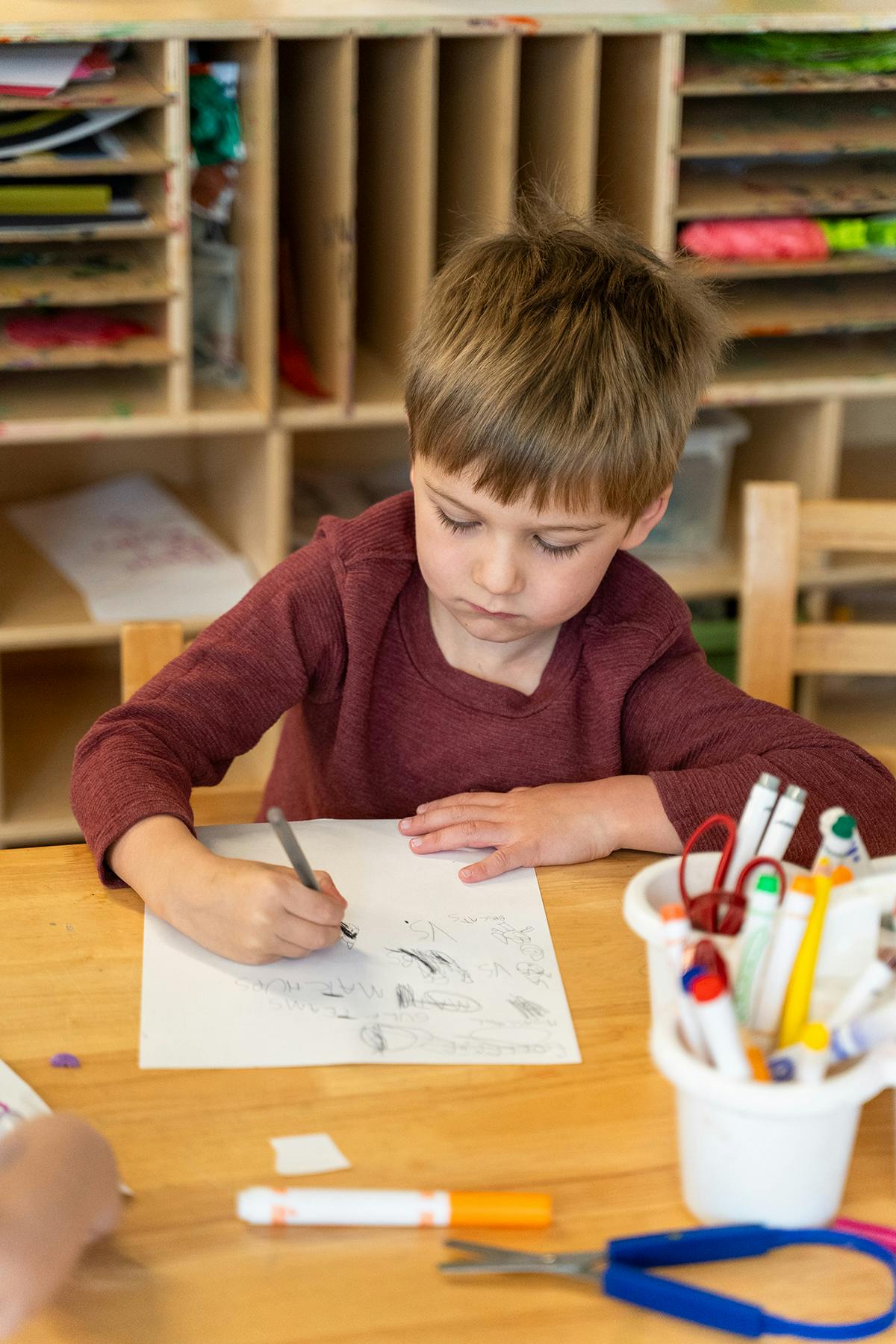 Child drawing on paper at a table in a classroom