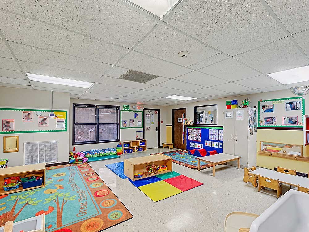 A colorful empty classroom with small tables, chairs, and play rugs